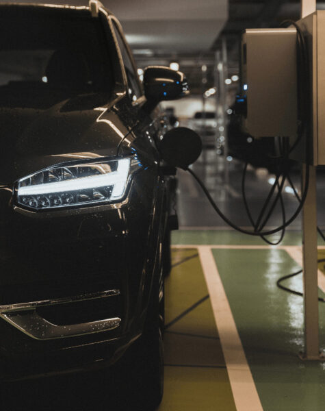 black car with headlights on on in underground car park plugged into EV charging point