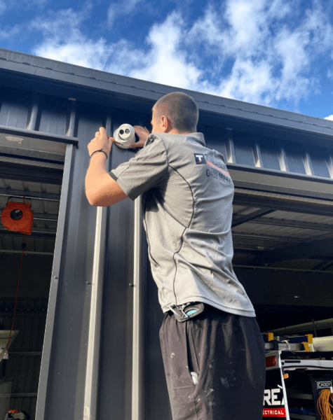 electrician on ladder installing security camera to outside of shed